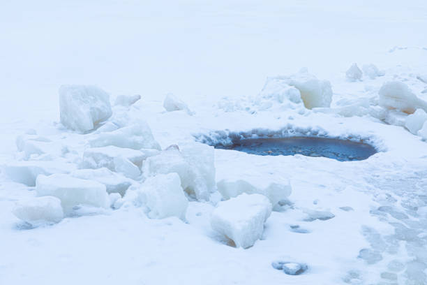 Beautiful winter landscape of bright, vivid and colorful ice hole among snow surface of lake, river or pound during snowfall or blizzard