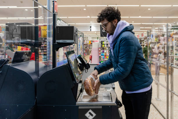 Self Service Checkout Side view of a man shopping in a supermarket while on a budget. He is scanning his items at the self service checkout in the North East of England. self checkout stock pictures, royalty-free photos & images