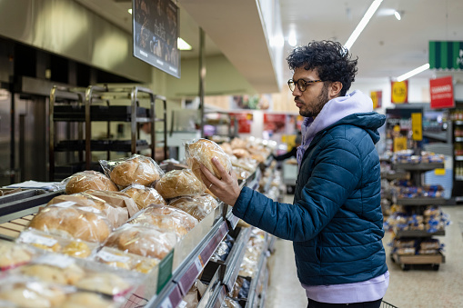 Man shopping in a supermarket while on a budget. He is looking for low prices on loads of bread due to inflation. He is living in the North East of England.