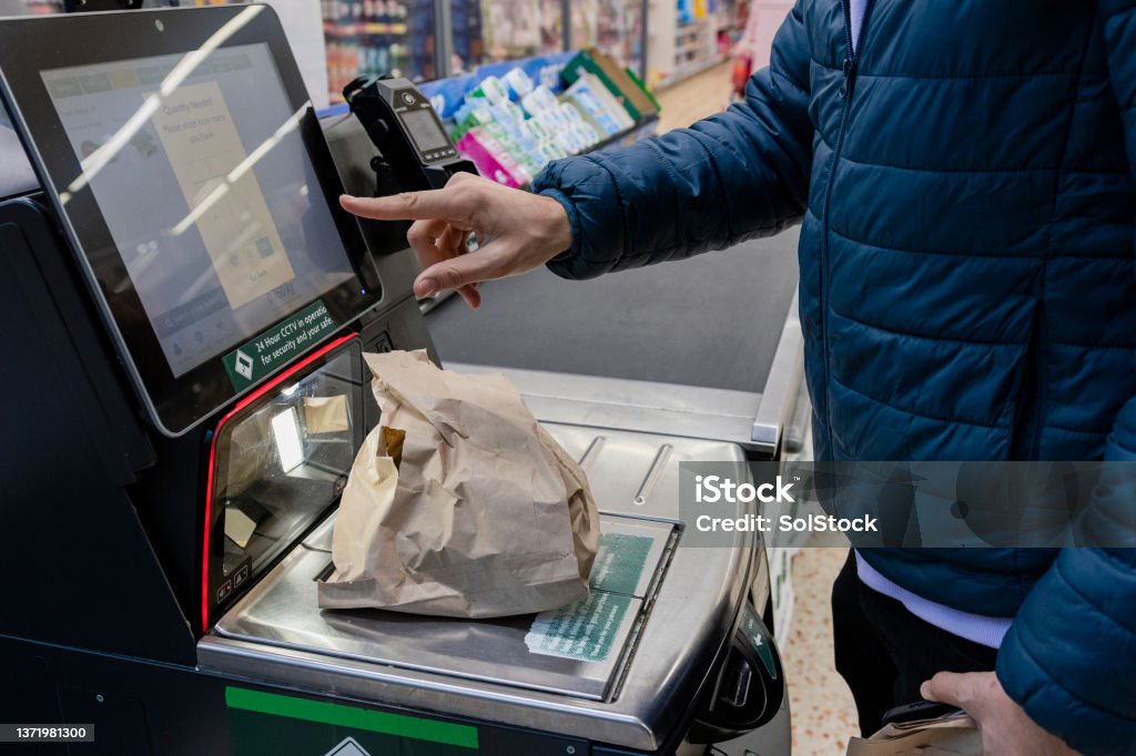 Weighing his Groceries to Check Out Side view of a man shopping in a supermarket while on a budget. He is weighing his loose items at the self service checkout in the North East of England. Self Checkout Stock Photo
