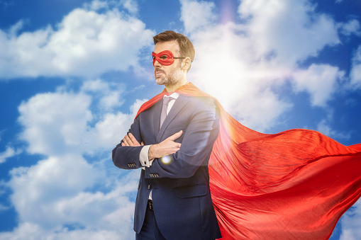 Super hero in red mask and cape posing. Sky background.  Helping hands. Handsome successful businessman. A lot of copy space.