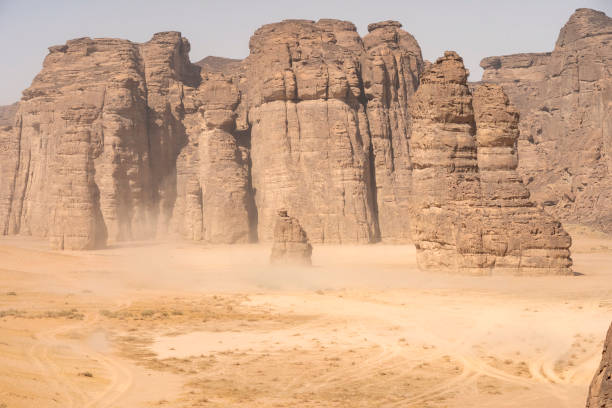 sand storm clouds on arid landscape with red-rock canyons and mountains background in the Sharaan natural desert of Al Ula in Saudi Arabia with grey stormy sky at the end of the day