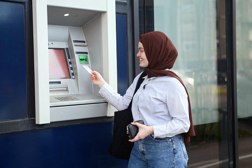 Arab woman using an ATM. About 25 years old, Middle-eastern female.