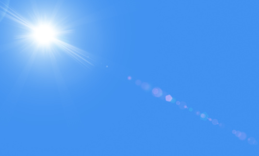 The bright white sun with rays against a blue sky without clouds.  Sun is in the upper left corner. There is a sunbeams with realistic lensflare representing heat and summer. There is a copyspace.