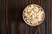 Bowl with popcorn on dark wooden table with copy-space flat view