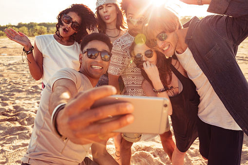 Image of excited young friends walking outdoors on the beach make selfie by mobile phone.