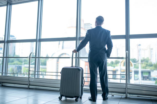 istock Man with suitcase standing looking at window in terminal 1371992760