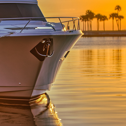 The front of a yacht with a chrome anchor in a calm sunrise lit harbor with palm trees in St. Petersburg, Florida.