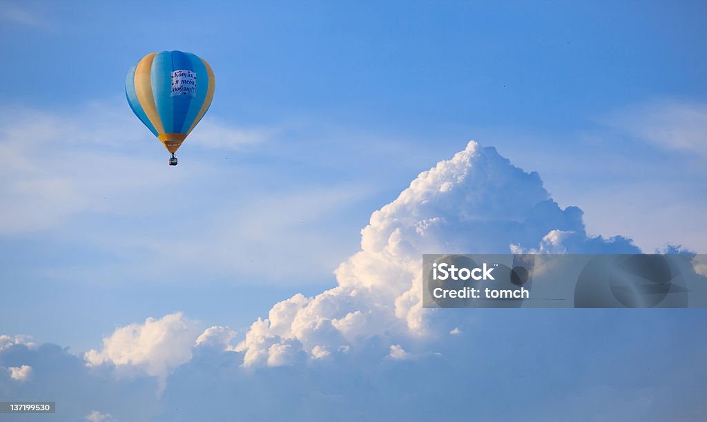 Yellow and blue hot air balloon floating in the cloudy sky Hot air balloon in the blue sky with clouds like mountains. On balloon is poster "I love you" on russian language Adventure Stock Photo