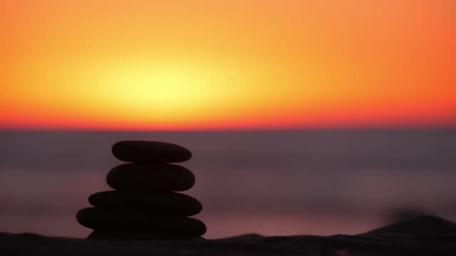 Stack of pebble stones, sandy ocean beach, sunset sky. Rock balancing by water.