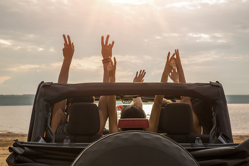 Back view of a group of happy friends sitting in a car with hands raised and having fun