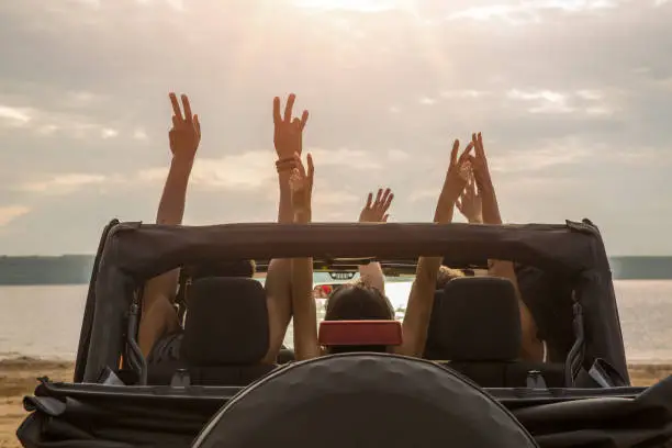 Photo of Friends sitting in a car with hands raised