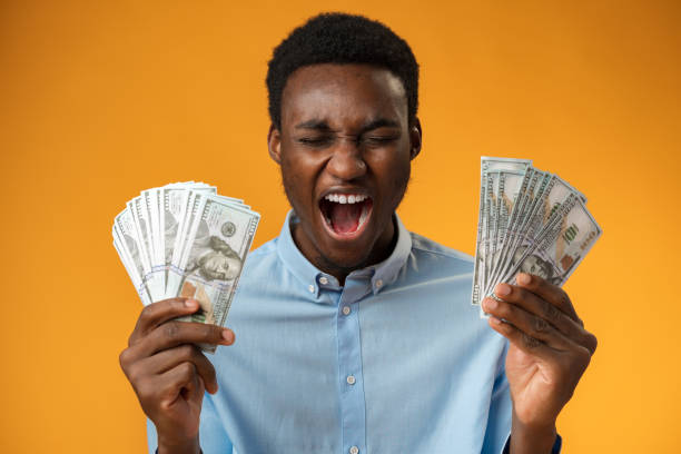 istock Excited black guy holding stack of Dollars in yellow studio 1372001059