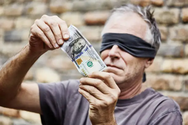 Photo of Blindfolded man tries to examine a US $100 banknote that he can't see