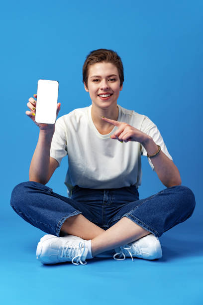istock Happy woman shows blank smartphone screen against blue background 1372002313