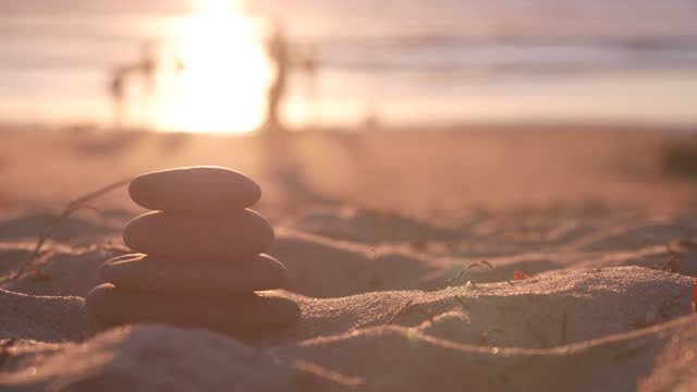 Stack of pebble stones, sandy ocean beach, sunset sky. Rock balancing by water.