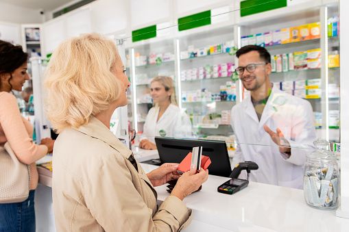 Pharmacist selling medications to senior female customer in the pharmacy store.
