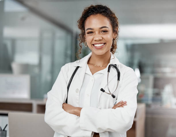 ritratto ritagliato di un'attraente giovane dottoressa in piedi con le braccia conserte in ufficio - camice da medico foto e immagini stock