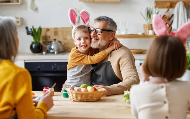 Photo of Happy family grandfather and little grandson holding wicker basket full of painted boiled eggs