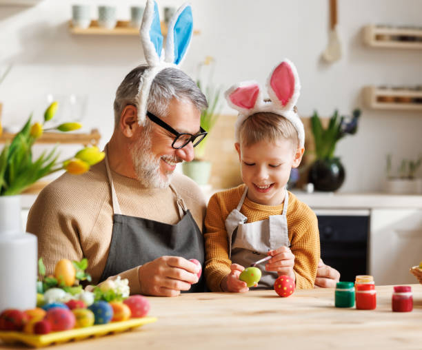 istock Loving grandfather and child in bunny ear headbands decorating eggs for Easter in light cozy kitchen 1372004109