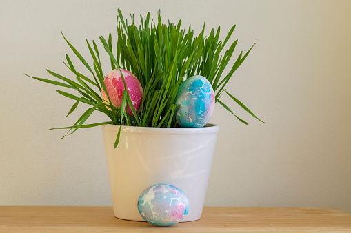 Colorful Easter pink red and light blue batik eggs in the grass in th pot, handmade homemade diy decoration on the table