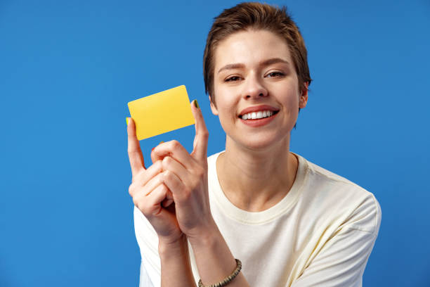 imagen de una mujer joven sosteniendo una tarjeta de visita con espacio de copia sobre fondo azul - invitation blank smiling business card fotografías e imágenes de stock