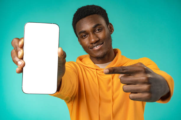 istock Smiling casual black man pointing at blank white cell phone screen in studio 1372006892