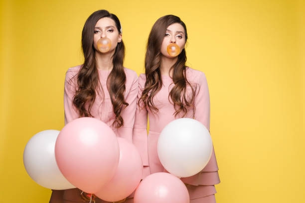 gemelos jóvenes sosteniendo globos rosados y blancos en sus manos. - chewing gum women bubble blowing fotografías e imágenes de stock