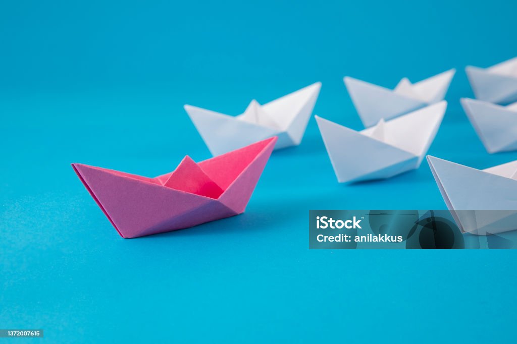 Red Paper Boat Leading Other Boats Red paper boat leading white boats on blue background Origami Stock Photo