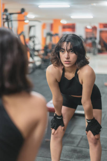 Young fitness woman looking in mirror after workout in gym. stock photo