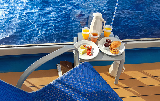 A colorful continental breakfast served on a balcony of a cruise ship at sea, with fruit, juice, breads and coffee.
