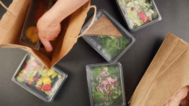 Taking food delivery in disposable containers from paper bags top view, take away meals, catering service, balanced nutrition. Fresh cooked portions in lunch boxes, vegetarian dishes. Healthy eating.