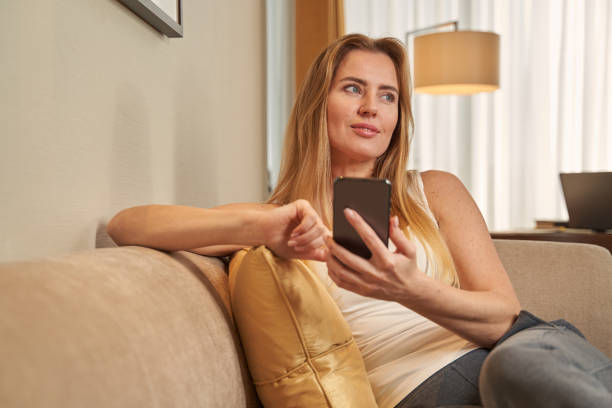 istock Young lady using smartphone on sofa in hotel room 1372012944