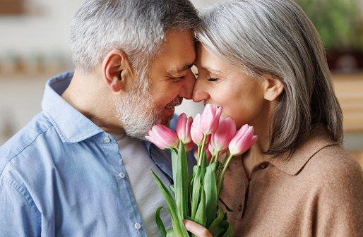 Elderly couple in love hugging on Valentine's day. A loving senior husband gives his wife a  tender bouquet of tulip flowers