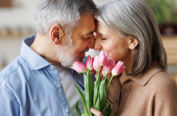 casal de idosos apaixonados se abraçando no dia dos namorados. um marido amoroso dá à esposa um buquê de tulipa - love embracing couple valentines day - fotografias e filmes do acervo