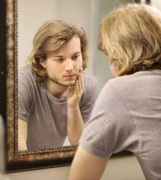 istock young man looking in the mirror,combing his hair,looking at problems on face. 1372021770