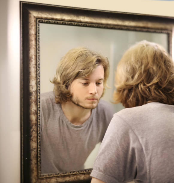 istock young man looking in the mirror,combing his hair,looking at problems on face. 1372021775