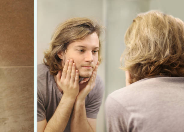 istock young man looking in the mirror,combing his hair,looking at problems on face. 1372021776