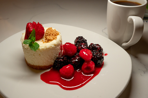 Homemade Gourmet Cheesecake Topped with fresh Strawberry and mint leave with blackberry and raspberry on the side