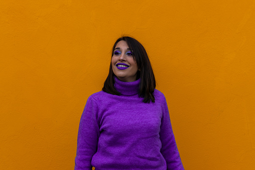 portrait of a happy young woman smiling looking at the camera dressed and made up in purple on yellow background