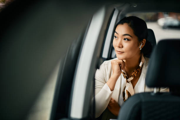Smiling Asian female CEO looking through the window while going on a business trip by car.