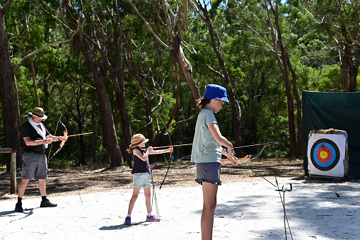 Father and daughters practicing archery together in the forest.