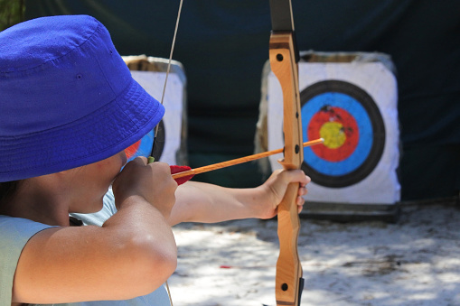 Rear view of young girl (female age 11-12) archer aiming to target.