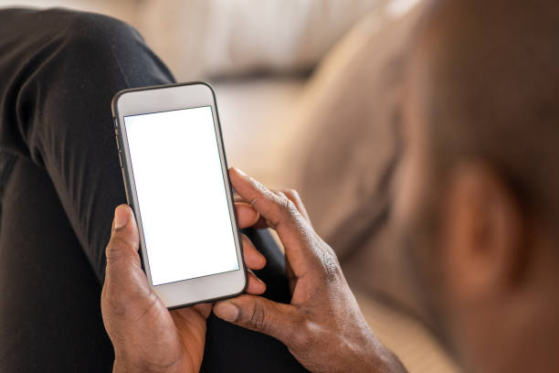 Close up of a black man's hands using a smart phone Close-up photo of a black man's hands using a smart phone with a white screen while lying on a couch. man looking at phone over shoulder stock pictures, royalty-free photos & images