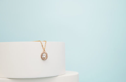 Hands of young female consumer holding golden chain with pendant hanging on grey velvet holder on display