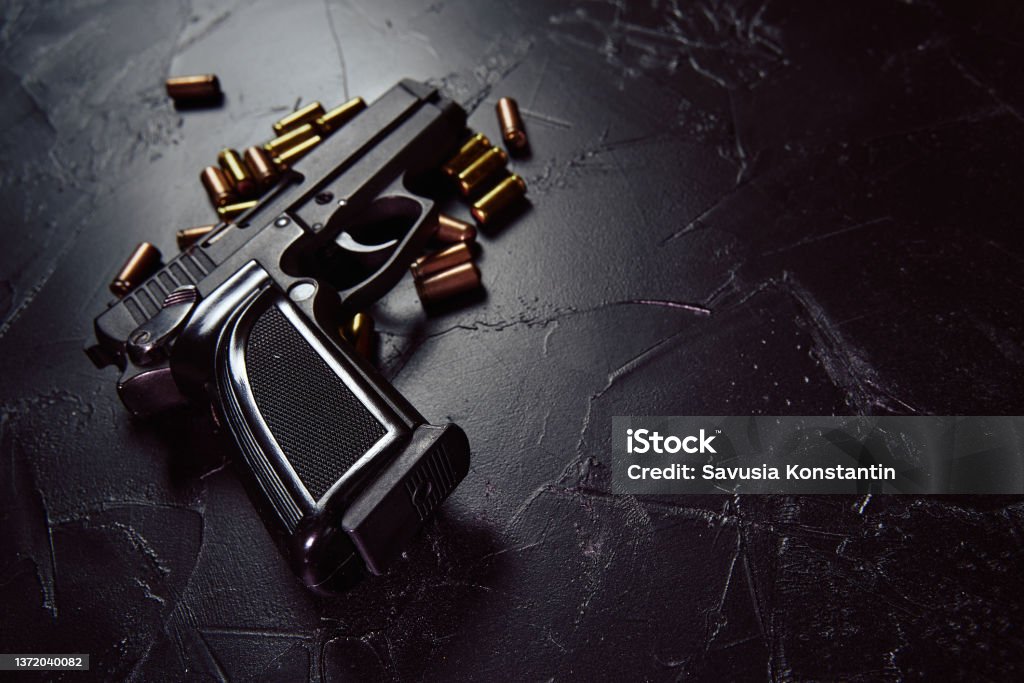 Pistol with cartridges on black concrete table. Black pistol with cartridges on table. Firearms on dark concrete table. Weapon of crime or defense. Automatic gun with bullets. Close up with copy space for text. Gun Stock Photo