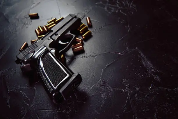 Photo of Pistol with cartridges on black concrete table.