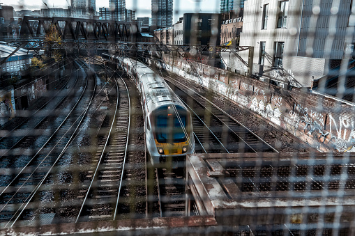 The view through the grid of the passenger train on the tracks leading to Liverpool Street Station. On both sides of the tracks, walls are covered with graffiti.