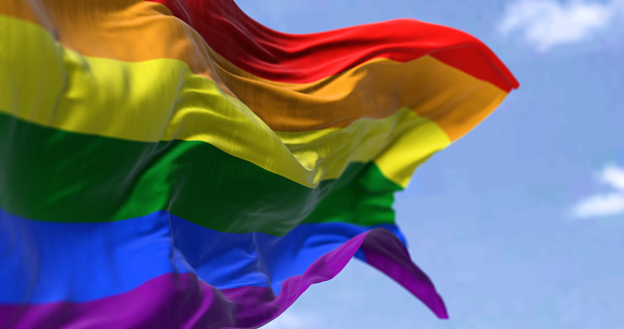 the rainbow flag waving in the wind in a clear day. Symbol of lesbian, gay, bisexual, transgender (LGBT) and queer pride and LGBT social movements. Selective focus