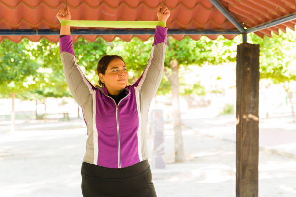 Happy plus size woman raising her hands and exercising with a resistance band. Smiling obese woman trying to lose some weight